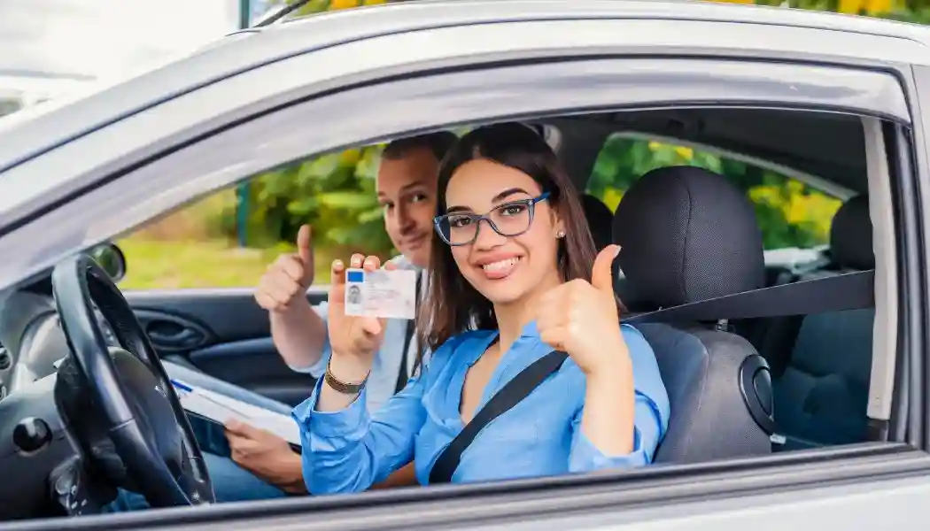 FOto de una alumna sonriente y el pulgar arriba posnado dentro del coche junto al carnet de conducir.