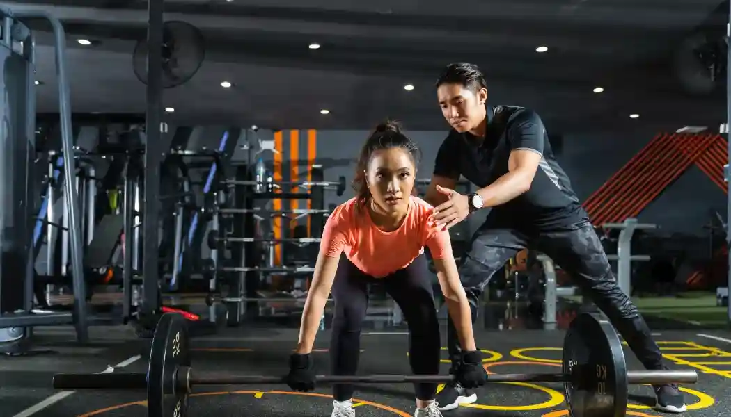 Foto de un entrenador personal ajustando la tecnica de una clienta.